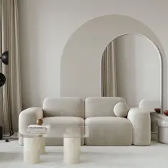 Nowoczesny salon z beżową kanapą i łukiem na ścianie. Lustro w kształcie łuku dodaje głębi.
