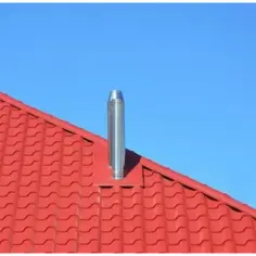 Metalowy komin na czerwonym dachu pod błękitnym niebem. Kluczowe jest utrzymanie prawidłowa temperatura spalin w kominie dla bezpieczeństwa.