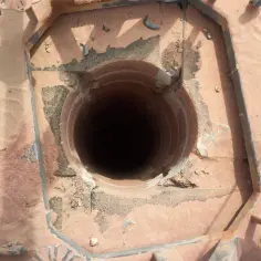 Widok z góry na otwór komina, gdzie widać ceramiczną rurę i metalową ramę. Trwa uszczelnienie rury kominowej.
