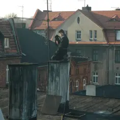 Kominiarz wykonuje przegląd kominiarski w mieszkaniu bez gazu, siedząc na dachu kamienicy.