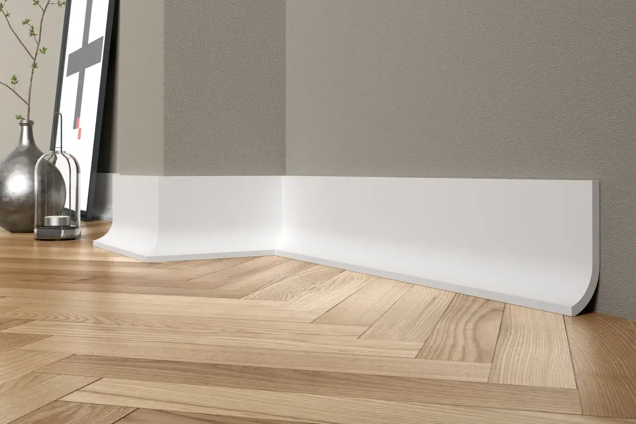 Białe, nowoczesne listwy przypodłogowe tworzą elegancką linię na drewnianej podłodze w jodełkę, podkreślając minimalistyczny wystrój wnętrza.