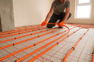 Instalator układa pomarańczowe rury systemu ogrzewania podłogowego na siatce. Idealna podłoga na ogrzewanie podłogowe.