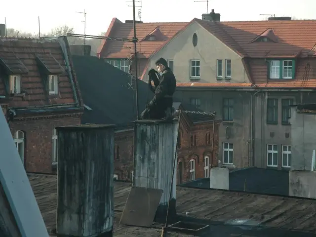Kominiarz wykonuje przegląd kominiarski w mieszkaniu bez gazu, siedząc na dachu kamienicy.